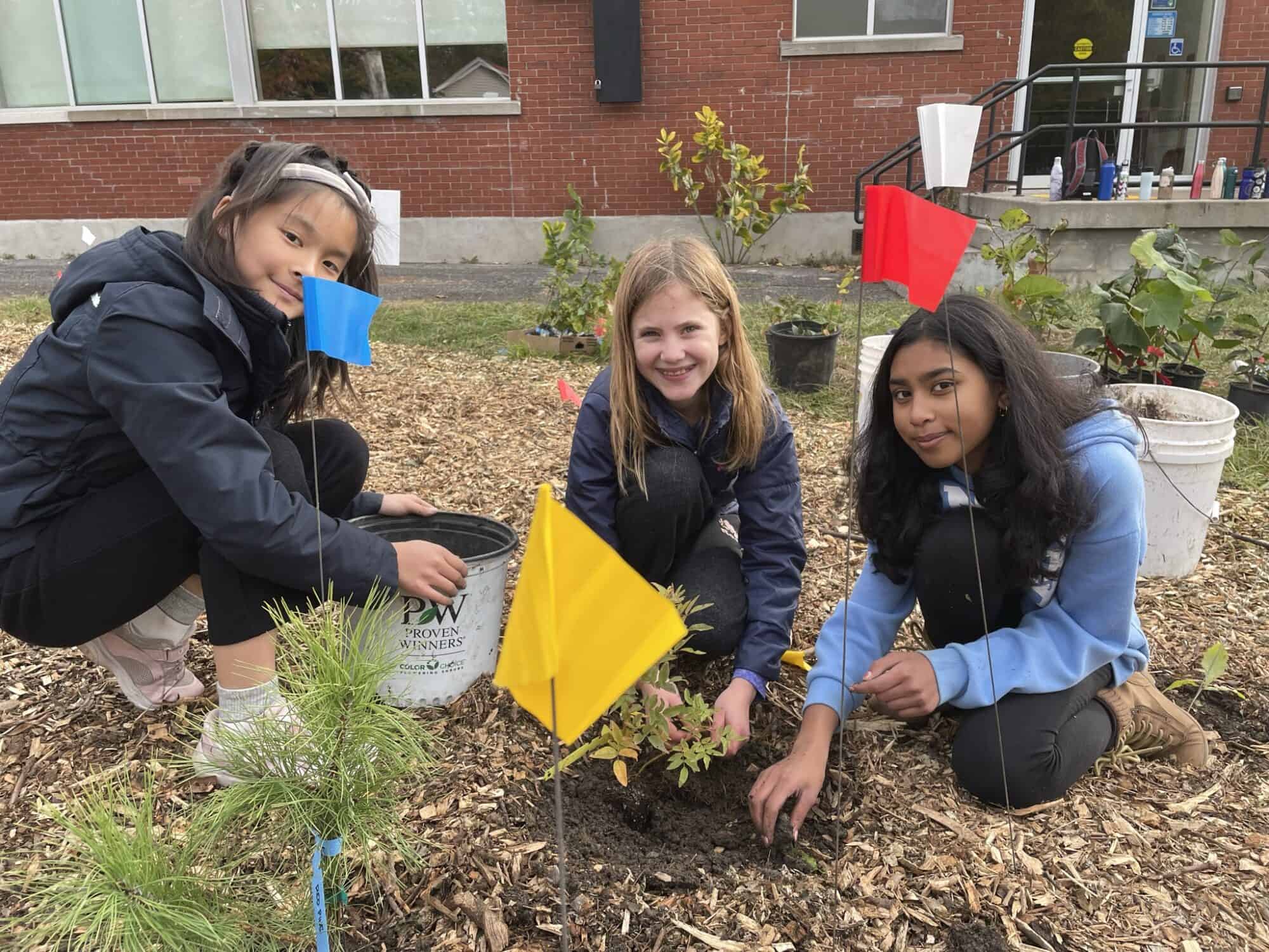 Children smiling and posing for camera while planting a mini forest.