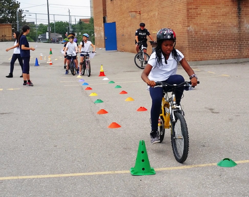 Group of kids participating in a cycling skills training session, each wearing helmets and riding bikes through a line of cones.