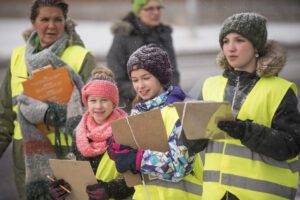 Children wearing winter clothing and safety vests hold clipboards while conducting a traffic count.