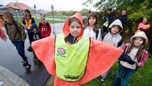 Children crossing a snowy street, led by a student in a safety vest.