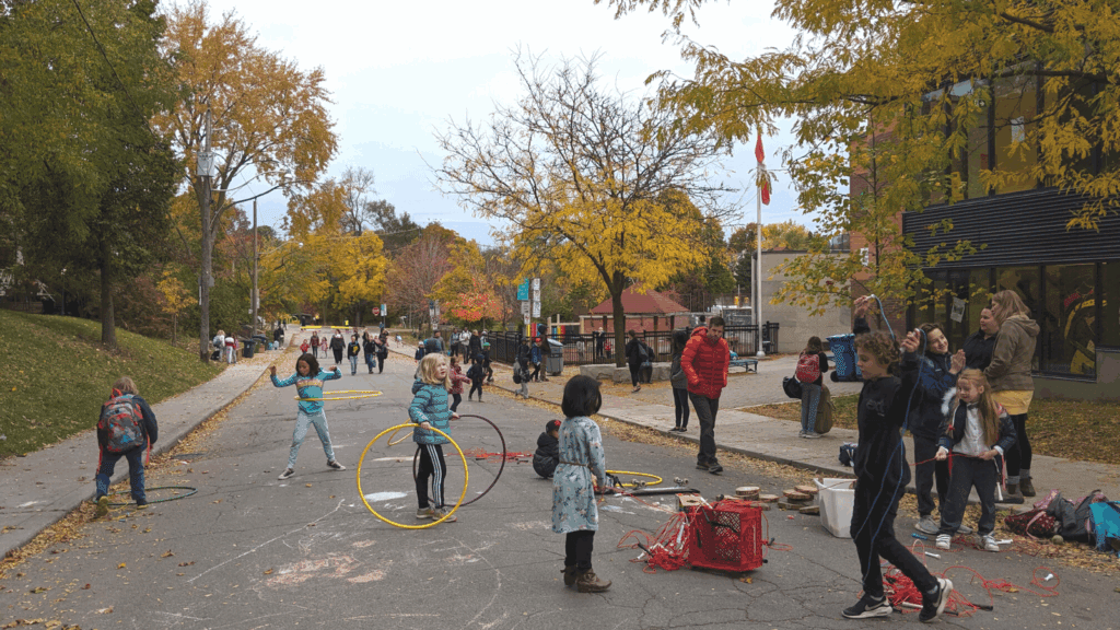 Children playing with hula hoops, skipping ropes, and chalk on a School Street in Toronto, Ontario.