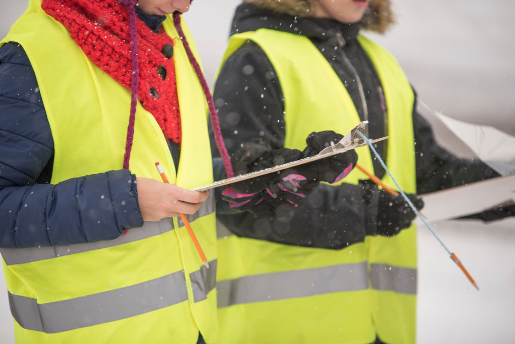 People in safety vests holding clipboards and pencils during a student travel survey.