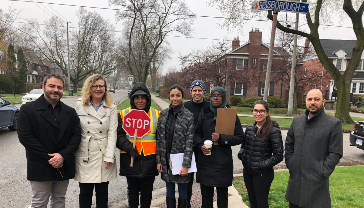 Group of adults on a residential street conducting a traffic observation, with one in a safety vest holding a stop sign.