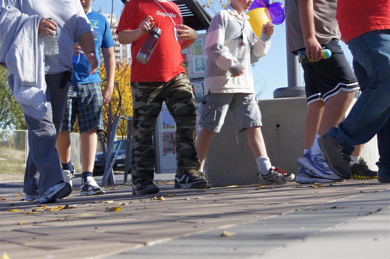 Group of children walking together outdoors, holding water bottles.