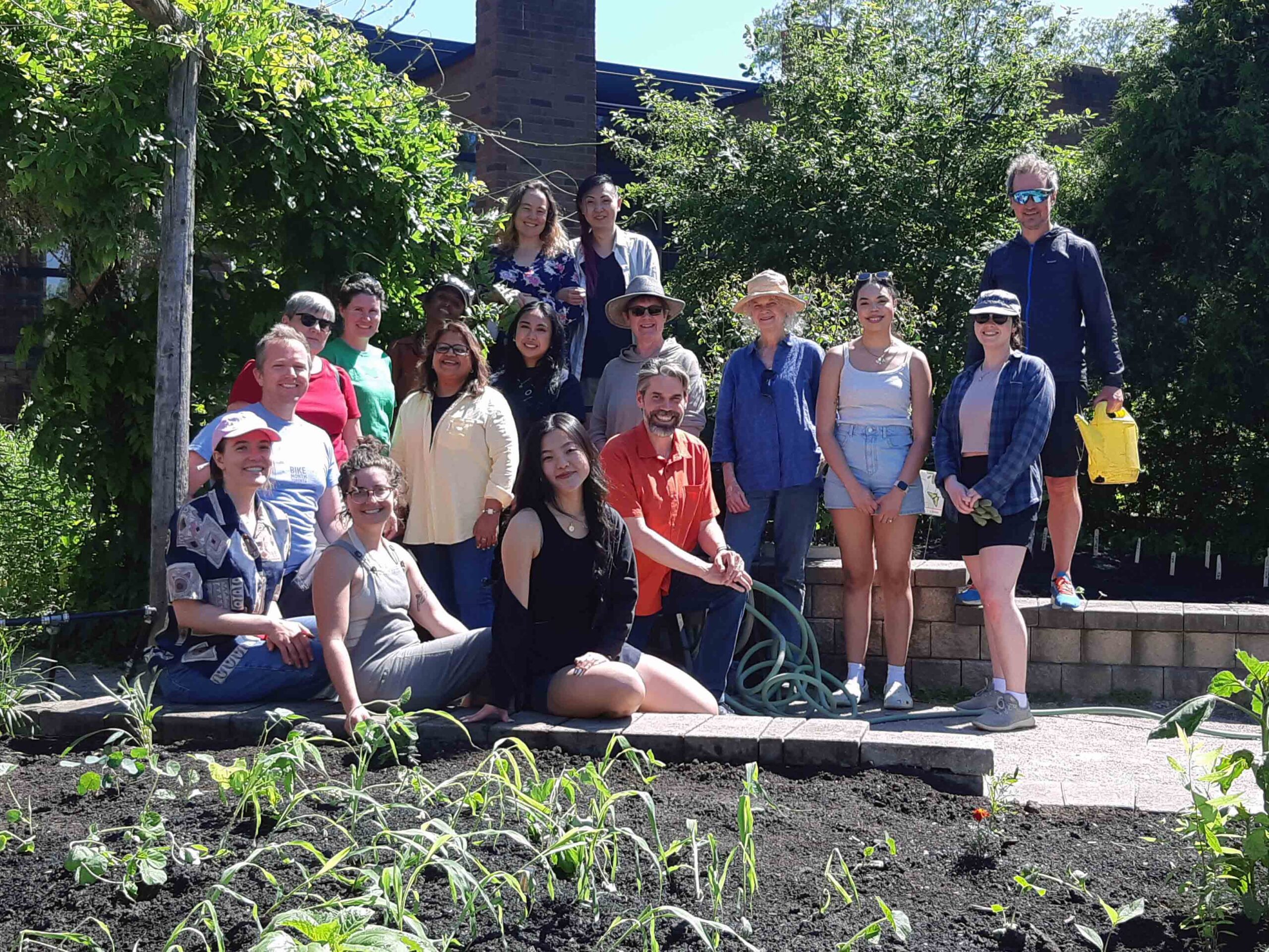 18 of GCC's staff team gathered in a garden amongst freshly planted corn, beans, and tomatoes.