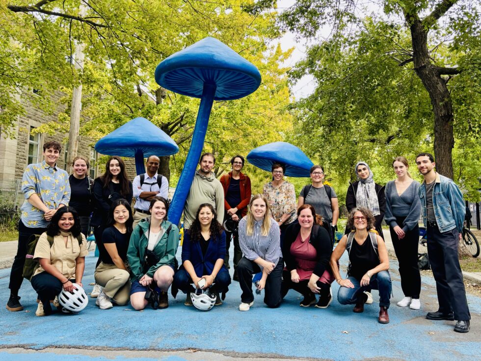 Group of diverse people from GCC's School Streets initiative gathered in front of giant mushroom monuments in a permanent school street in Montreal.
