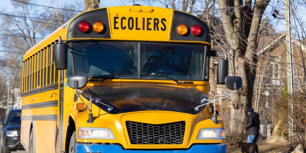 Yellow school bus with French “Ecoliers” on top and a blue front bumper identifying this is an electrified school bus.