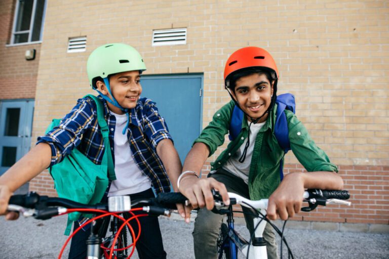 Two kids on their respective bikes, wearing helmets, and smiling at the camera.